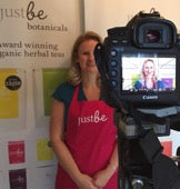 Gail Bryden founder of JustBe Botanicals standing behind a camera recording her pitch for virgin media voom competition