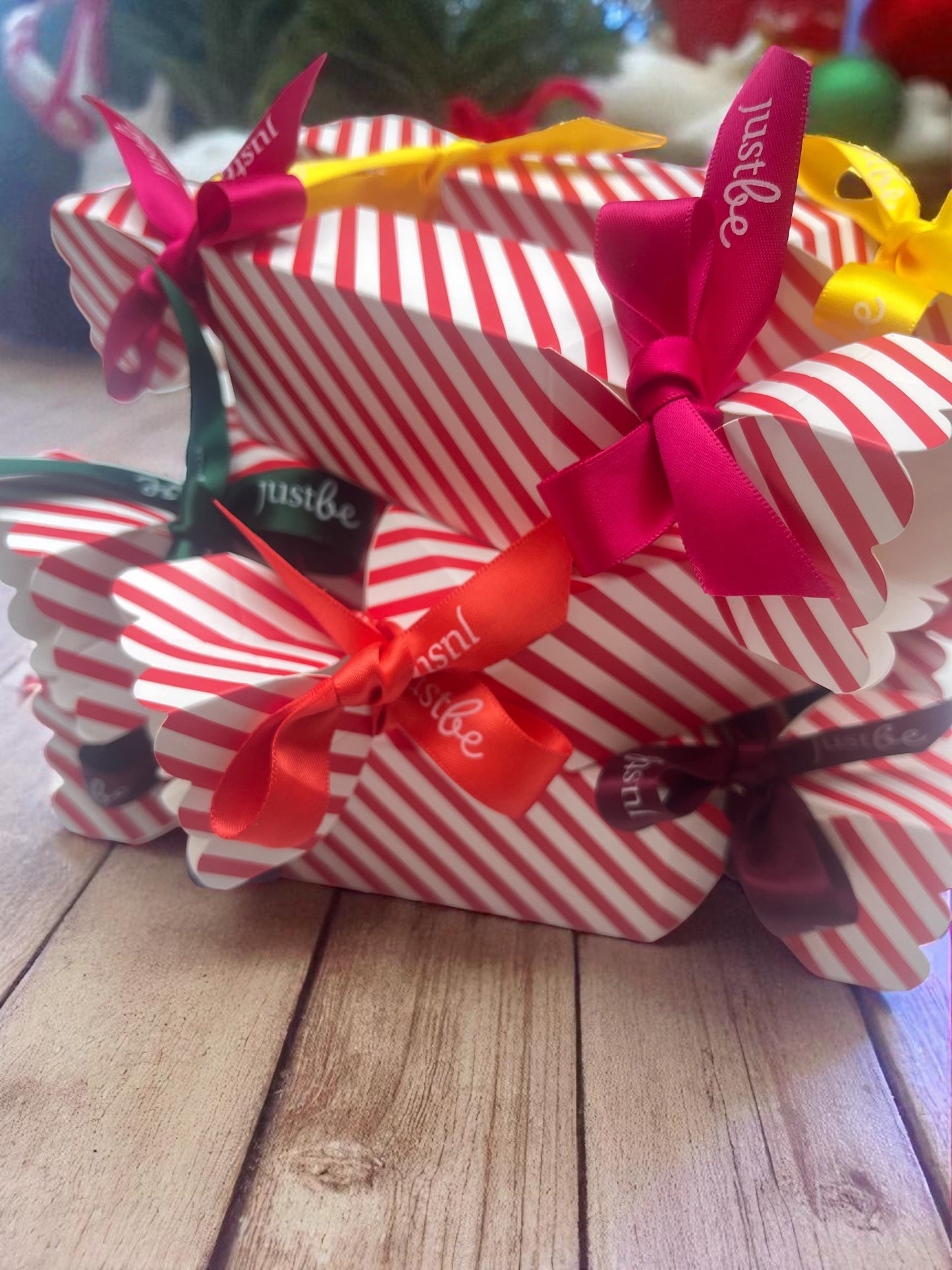 Red and white striped Christmas crackers with colorful JustBe ribbons on a wooden surface