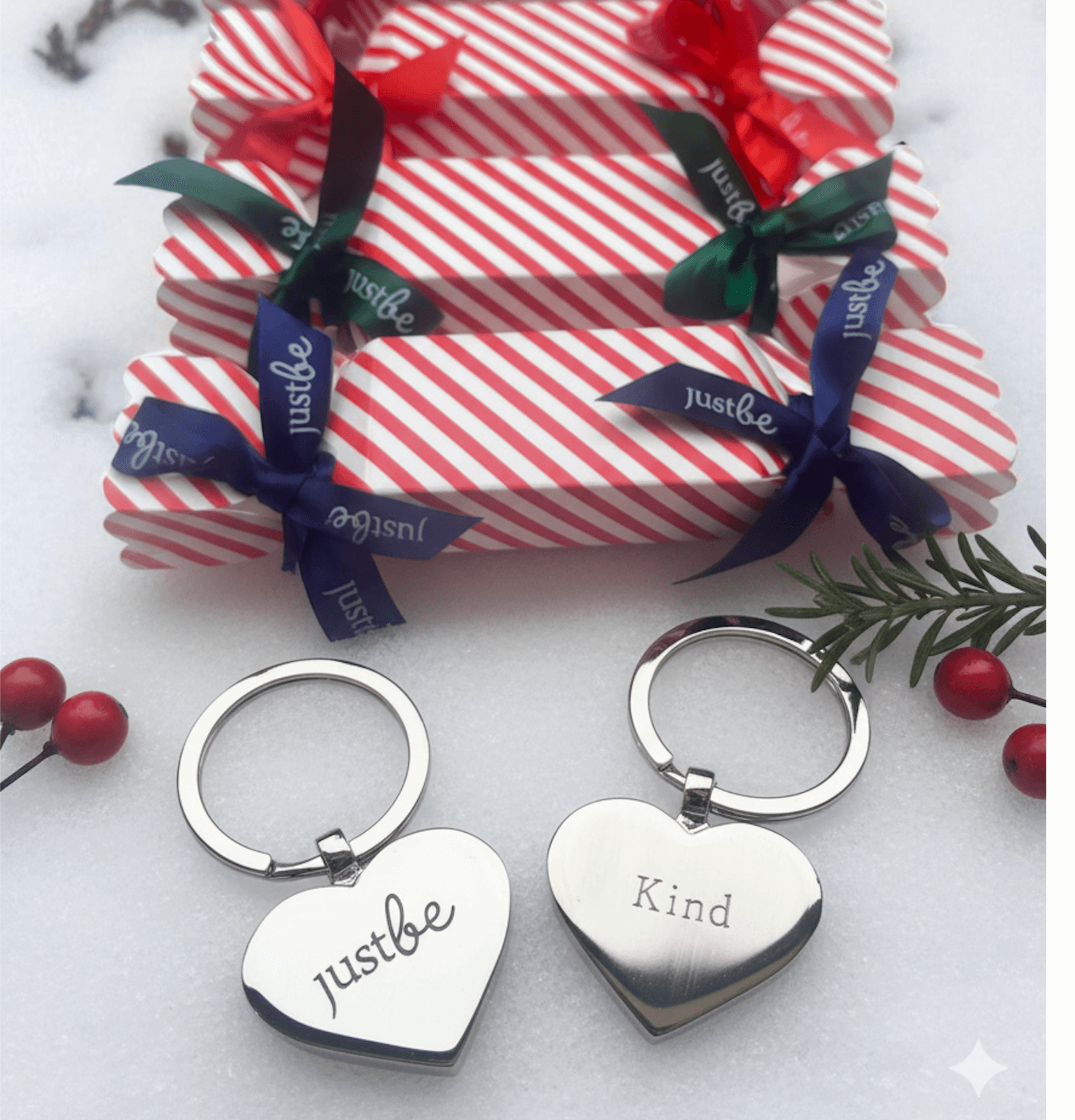 Heart-shaped keychains with engraved text next to red and white striped Christmas crackers with ribbons on snow.