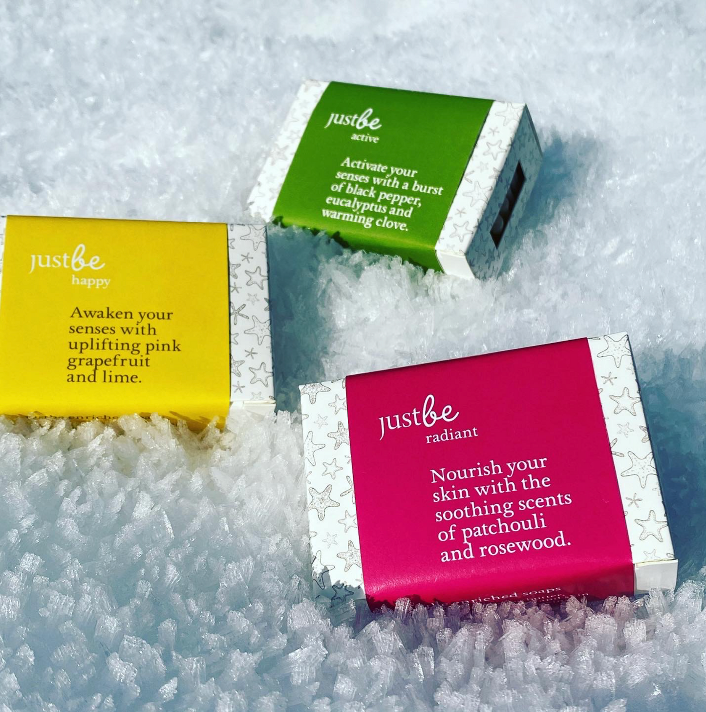 Three bars of JustBe soaps on a snowy surface