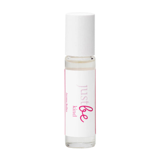 JustBe Kind pulse point oil: a comforting aromatherapy blend with mandarin and bergamot  to soothe and support emotional wellbeing. In a clear bottle with a white lid. The label is white with pink writing.