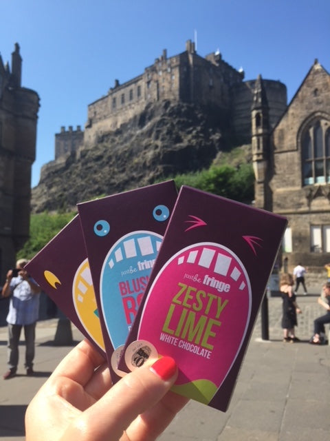 3 JustBe Fringe chocolate bars being held in front of Edinburgh Castle