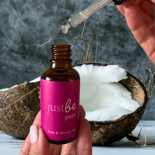 JustBe Pure Body & Massage Oil bottle with dropper and fresh coconut background