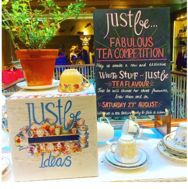 Wooden box with JustBe ideas drawn on the front sitting beside a blackboard detailing the JustBe Fabulous Tea Competition at White Stuff store Edinburgh