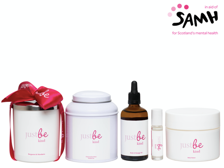 JustBe Botanicals Kind wellbeing range in support of SAMH: five white and pink-labelled products including a candle, tea tin, oil dropper, aroma roller and body butter displayed alongside the SAMH logo.