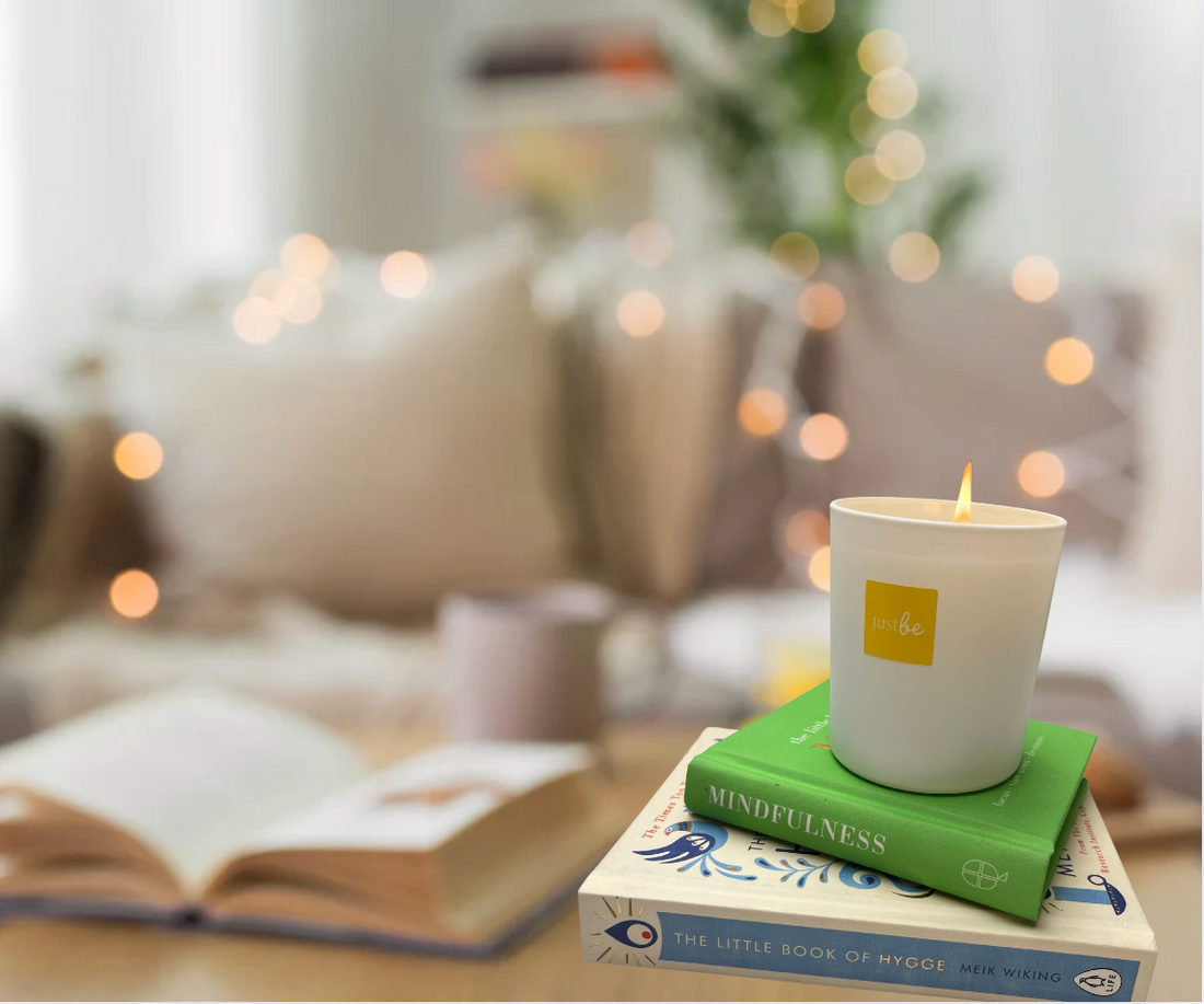 JustBe Happy candle sitting on top of two books in a cosy living room