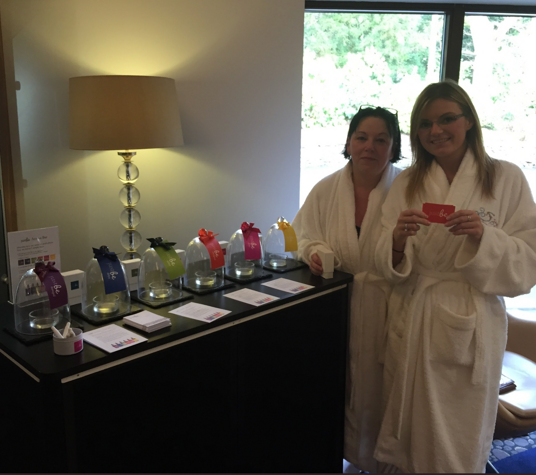 Two ladies in a spa wearing white robes standing in front of JustBe Botanicals scent bar