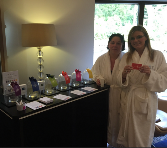Two ladies in a spa wearing white robes standing in front of JustBe Botanicals scent bar