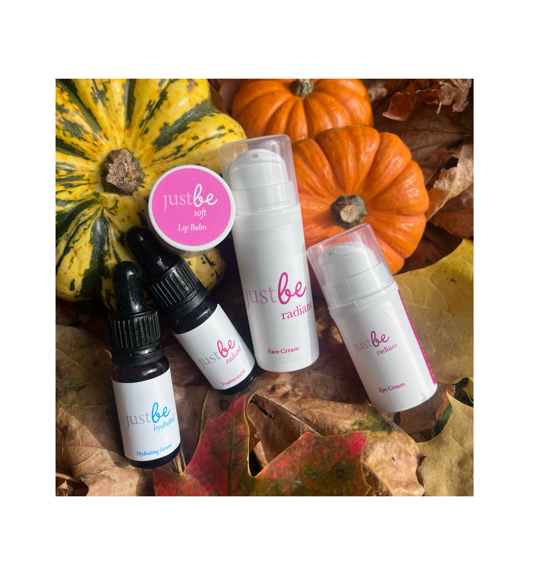 JustBe Botanicals Hydrating Serum, Treatment Oil, Face Cream, Eye Cream and Lip Balm among autumn leaves and pumpkins.