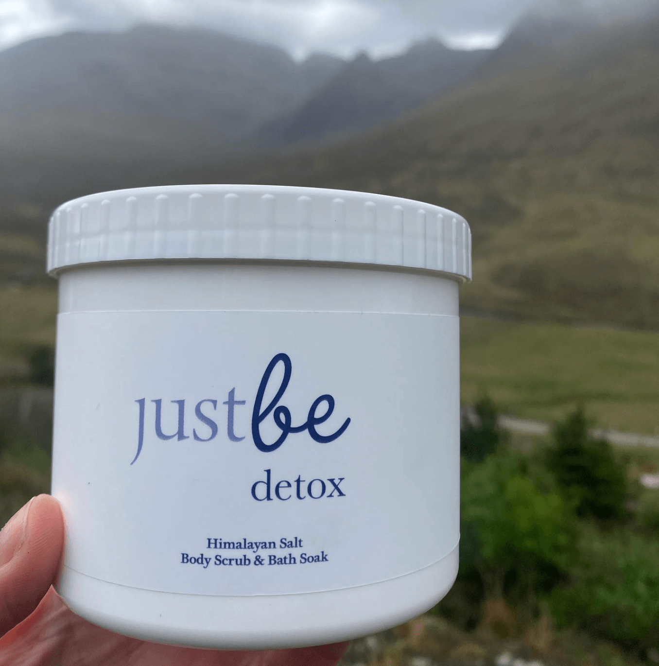 Container of 'just be detox' product held in front of a mountainous landscape Skye Scotland