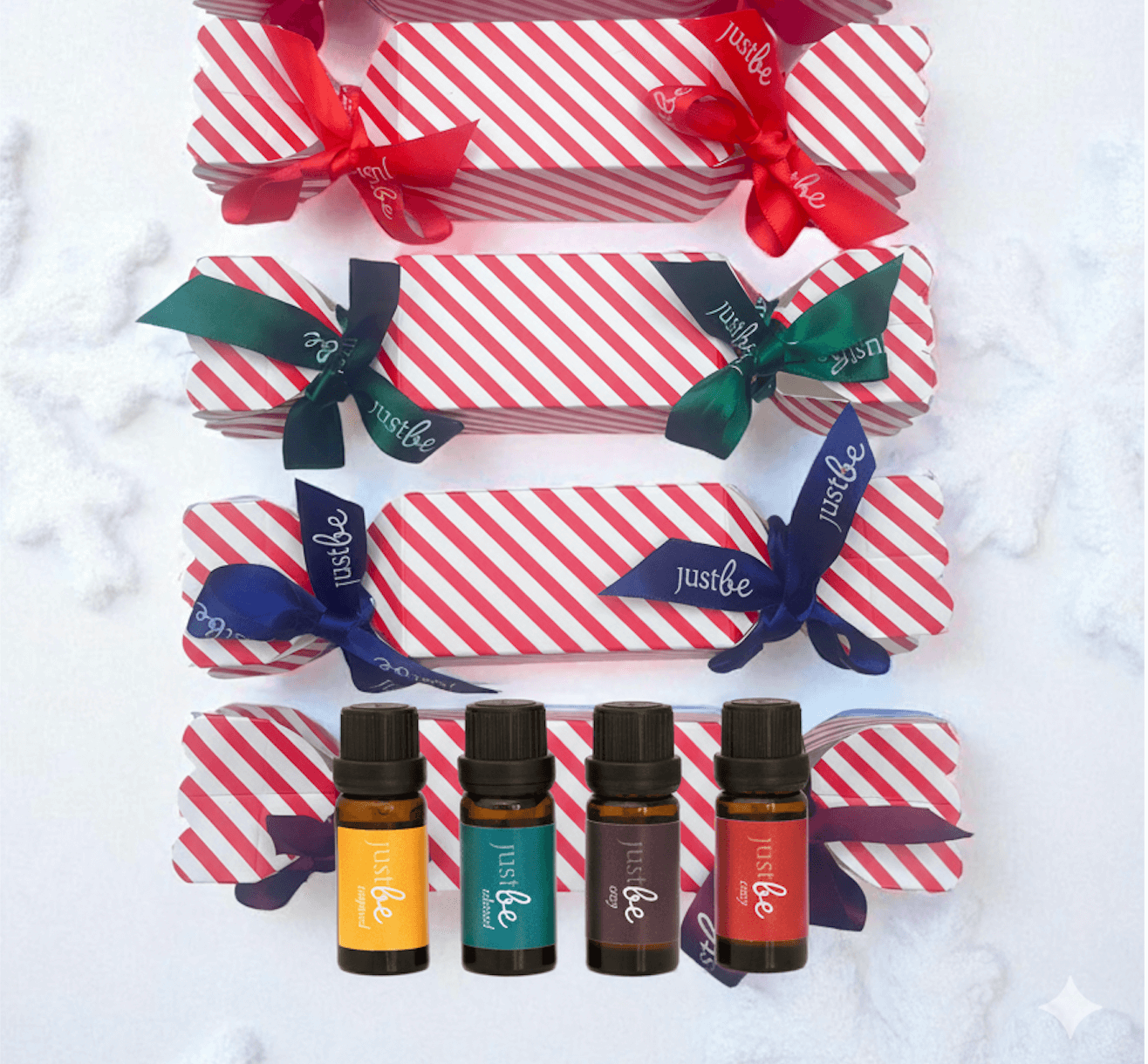 Set of JustBe essential oil bottles with red and white striped Christmas crackers on a snow background
