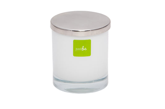 Glass candle with a silver lid and green 'just be' label on a white background