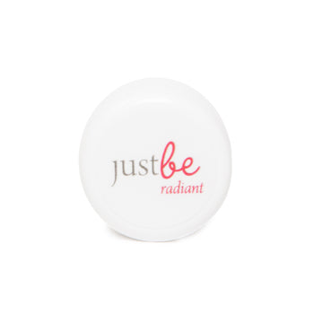 A small white sample pot of JustBe Radiant Eye Cream with the JustBe logo in grey and pink, and the word "radiant" in pink underneath.