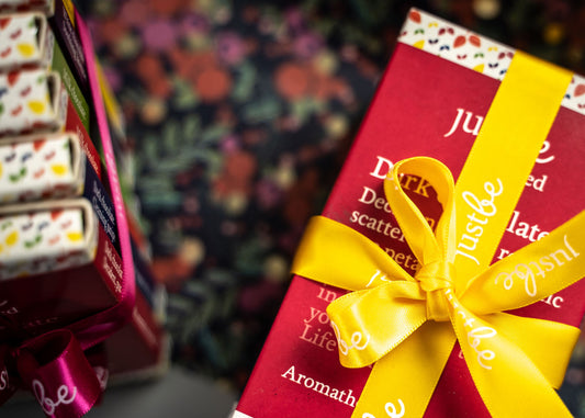 A package of JustBe Aromotherapy chocolates with a yellow and red design, tied with a yellow ribbon.