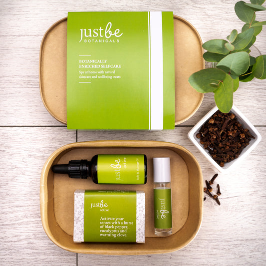 JustBe Active Body Gift Set, including a body & massage oil, aromatherapy rollerball, and natural soap bar all with green-labels packaged in a kraft box with a green JustBe Botanicals sleeve. Surrounded by eucalyptus leaves and whole cloves for a fresh, energising feel.