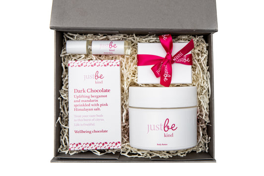 A gift set containing an aroma roller, keyring, body butter, and a bar of dark chocolate, packaged in a box with 'JustBe Kind' branding.