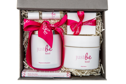 JustBe Kind gift set with 5 items: Aroma Roller, Bergamot & Mandarin Candle, bar of chocolate white box with pink ribbon containing a keyring and Body Butter