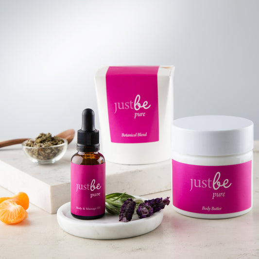 Gift set featuring JustBe Pure herbal tea, body & massage oil, and body butter, styled with fresh lavender, mandarin, and a dish containing raspberry leaves