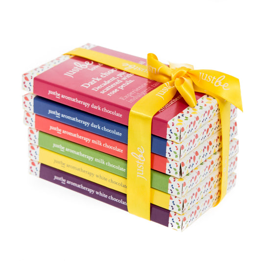 A set of six JustBe Aromatherapy Chocolates, each with a different color packaging representing different flavors, tied together with a yellow ribbon.