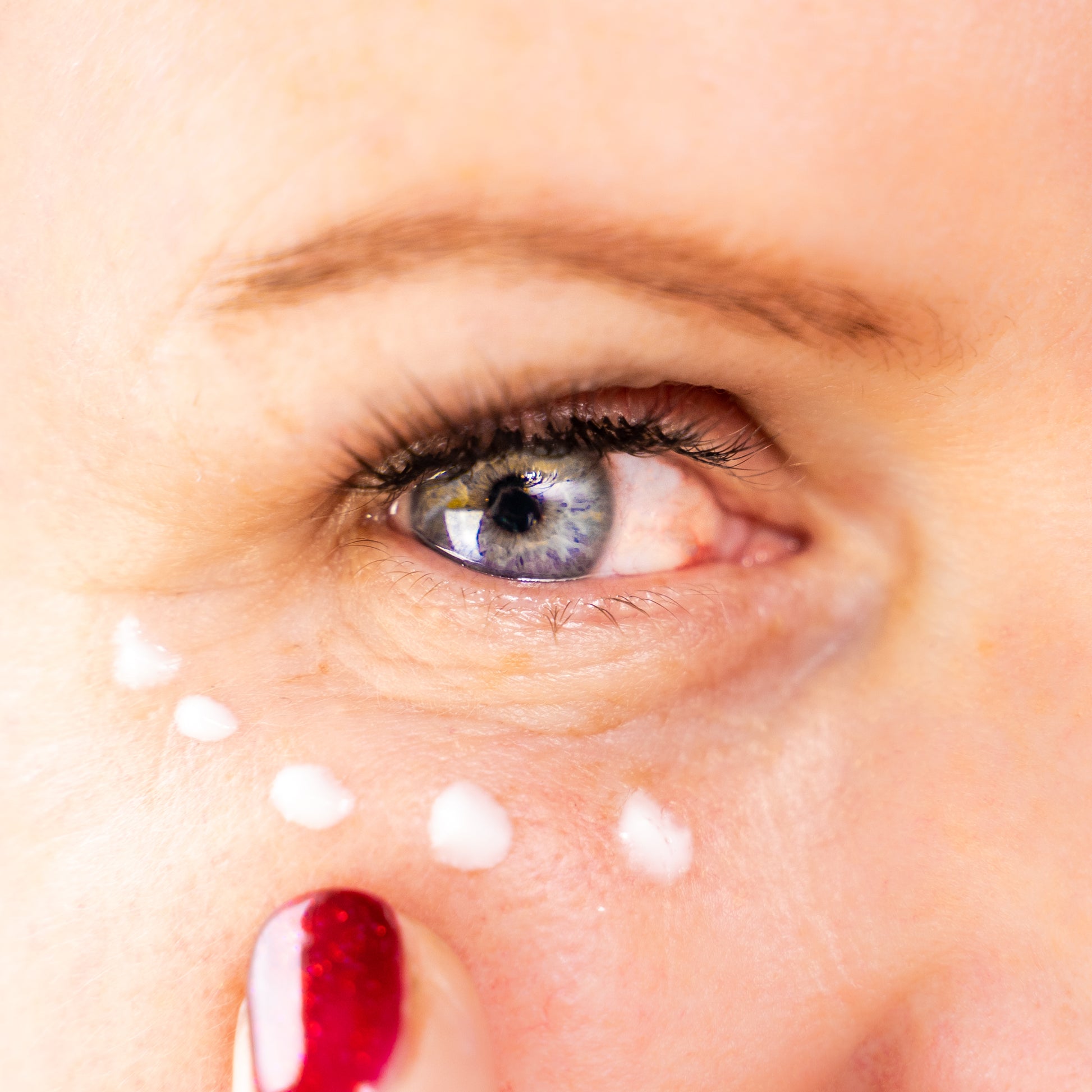 Close-up of a woman applying JustBe Radiant Eye Cream under the eye area with fingertips, showing targeted hydration for fine lines and puffiness.